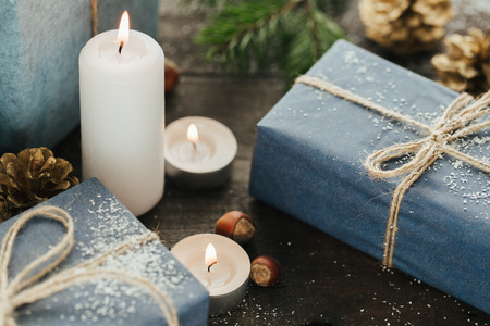 Festive Gifts with Boxes, Candle, Snow, Coniferous, Basket, Cinnamon, Pine Cones, Nuts on Wooden Background. With space for your textの写真素材