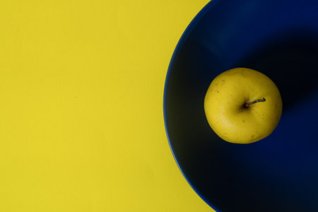 Top view of fresh yellow apple on a blue plate with yellow copy spaceの写真素材