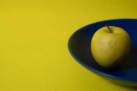 Fresh yellow apple on a blue plate with yellow copy space