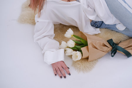 Woman in white shirt lying next to a bouquet of white tulipsの写真素材