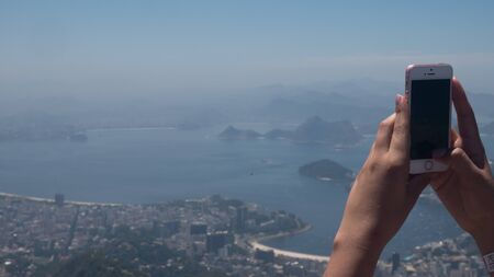 Woman taking photos with cellphone from Corcovado in Rio de Janeiroの写真素材