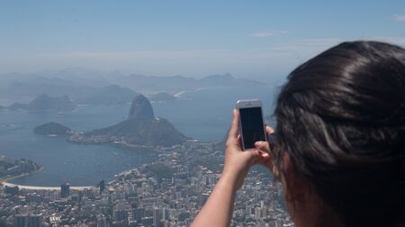 Woman taking photos with cellphone from Corcovado in Rio de Janeiroの写真素材