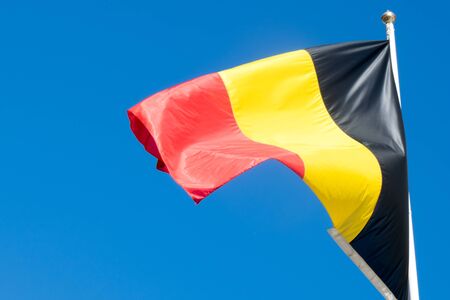 Belgium national flag on flagpole on blue sky backgroundの写真素材