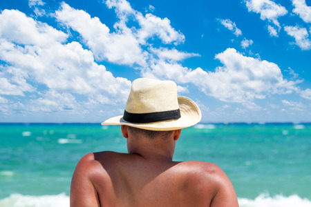 Back view of a man with hat relaxing at tropical beachの写真素材