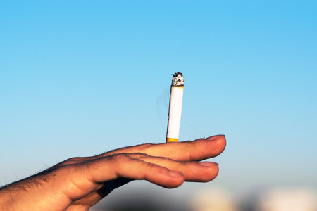 Male hand holding cigar outdoors against blue skyの写真素材
