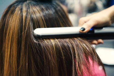 Hairdresser using hair straightener on brown-haired womanの写真素材