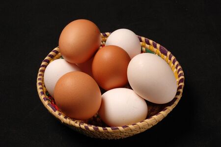 Eggs in basket on table against black backgroundの写真素材