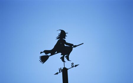 Witch shaped wind vane against blue skyの写真素材