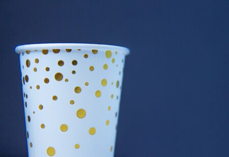 Paper cup with golden dots on a blue background. Side viewの写真素材