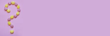 Multicolored candy in the form of a question mark on pink background. Banner with copy space. Flat...