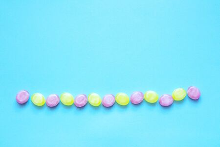 Multicolored candy laid out in line on a blue background. With copy space. Flat lay