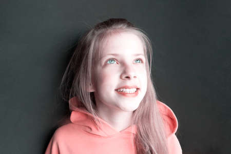 Teenager girl in an pink sweatshirt with bright emotions on her face on a black background. Joyful...