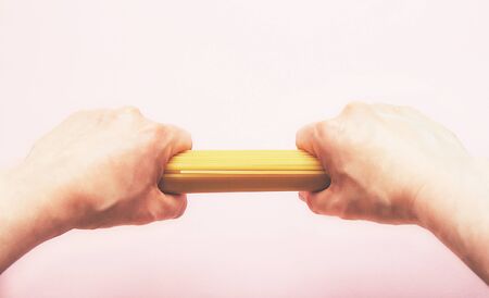 Raw spaghetti isolated on pink background. Pasta. Stay home cooking. Hands holding spaghetti. Selective focusの写真素材