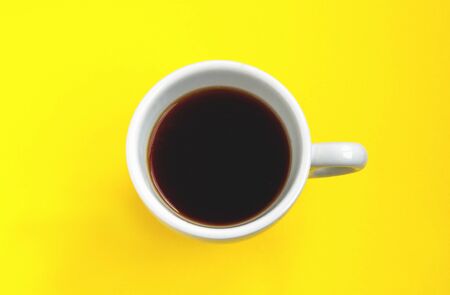 Black coffee in a white cup isolated on a yellow background. Selective focus. Top viewの写真素材