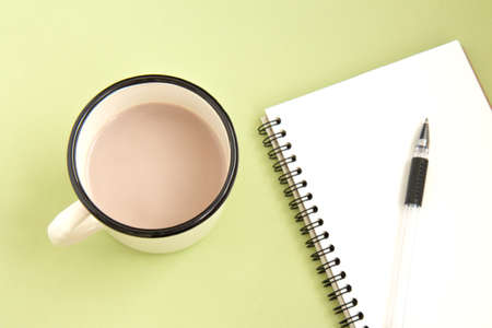 Open white notebook with pen and iron white cup with cocoa on a delicate green background. Flat lay. Selective focusの写真素材