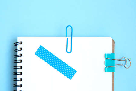 White open notebook with blue paper clip, clip and piece of tape on blue background. Blue set. Stationery on a blue background with space for text. School stationery. Back to school. Flat layの写真素材