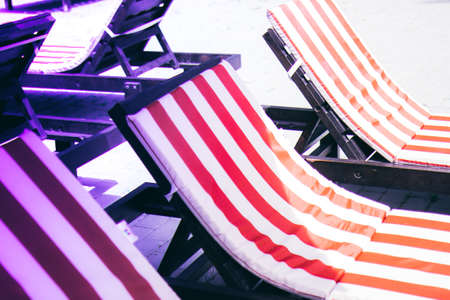 Striped red and white loungers near the swimming pool on a summer day. Sun chairs at the pool with neon lightsの写真素材