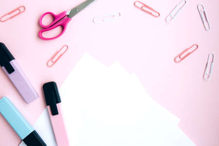 White notepad, pink, blue and green markers, paper clips, scissors, eraser on pink background with space for text. School stationery. Back to school, creative workspace. Set of colorful stationeryの写真素材