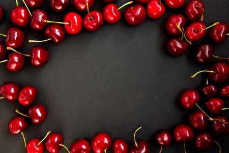 Red, ripe cherries on a black background, in the middle place for your text. Cherries isolated on...