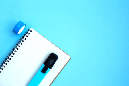 White open notebook with blue marker and  on a bright blue background. Stationery on a blue...