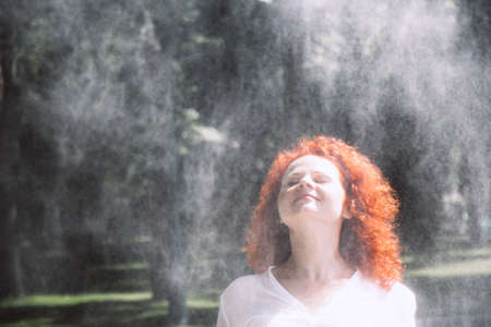 Young woman with curly, red hair framed her face under refreshing drops of water. Beautiful female...