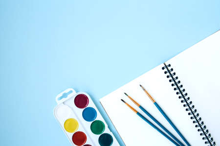Back to school flat lay with watercolor and open notepad on blue background with space for text....