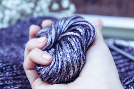 Needlework. Texture beautiful knitted bright violet fabric with metallic fibers and knitting needles and clew as background. Woman's hand holding a clew. Female hobby conceptの写真素材