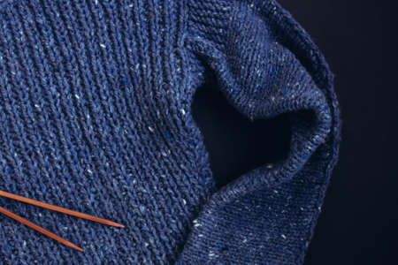 Blue knit sweater and knitting needles on dark black background. Heart shape. Craft on black background. Texture beautiful knitted fabric as background. Female hobby conceptの写真素材