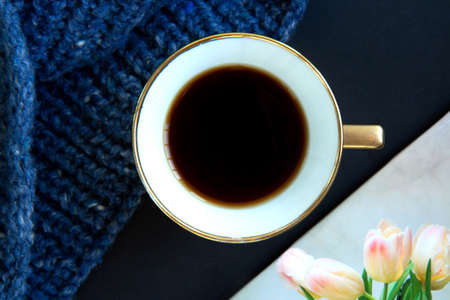 Blue knit sweater, porcelain gold cup with coffee and notepad on black background. Knitwear as a concept of female hobbyの写真素材