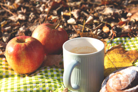 Autumn still life. Red, ripe apples, a cup of hot coffee with milk in a blue cup, sweet cinnamon bun...