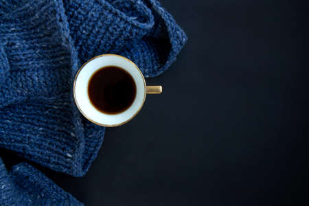 Blue knit sweater, porcelain gold cup with coffee on black background. Knitwear as a concept of...