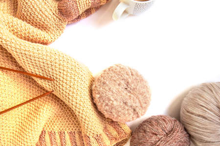 Balls of woolen yarn of nude colors and a knitted beige sweater, knitting needles, cup of coffee on...