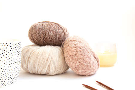 Three balls of delicate yarn and knitting needles and a burning candle on a bright background. Craft...