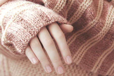 Woman in a beige soft warm knitted sweater folded her hands in the sunlight. Autumn soon