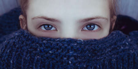 Beautiful girl with blue eyes wrapped herself in a warm blue knitted sweaterの写真素材