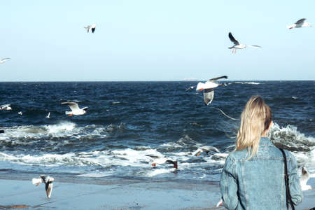 The blonde girl looks at the ocean. Stormy sea, ocean and background many seagulls soar in the sky....