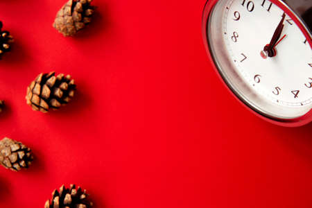 Beautiful vintage silver alarm clock and spruce cones on a bright red background. Time concept