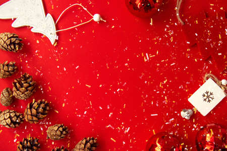 Spruce cones, red Christmas balls, silver bell and white and red Christmas tree on a bright red background with multicolored glittering confettiの写真素材