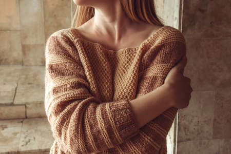 Female hugging herself with arms. Young woman in a cozy beige sweater spends time outdoors....
