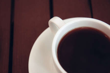 Black coffee with foam in a white ceramic cup on a wooden table. Selective focus. Breakfast in a cafeの写真素材