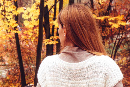 A young woman in a white warm, cozy, knitted sweater walks in the autumn park, forest. Beautiful...