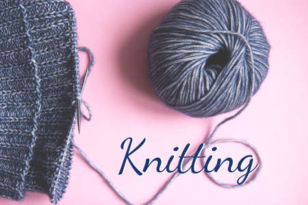 Knitting project underway. Knitting with a ball of blue yarn and knitting needles on pink background with the inscription knitting. Woman knitting woolen clothesの写真素材