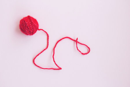 One red ball of woolen thread with long twisted thread on a pink background with copy space