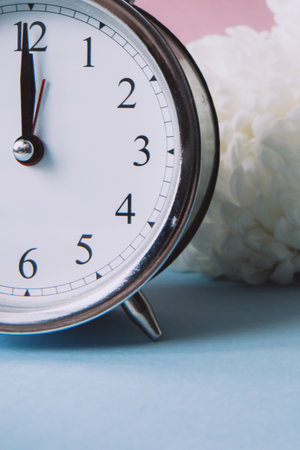 Beautiful vintage silver alarm clock and white peonies on a pink and blue background. Time concept. Holiday routine. Side view, copy spaceの写真素材