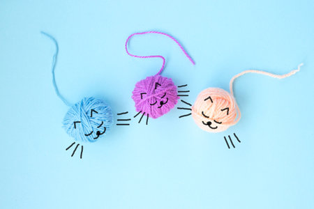 Three skeins of colorful woolen yarn with drawn details is presented in the form of a cute kittens on a light blue background with copy space. Close upの写真素材