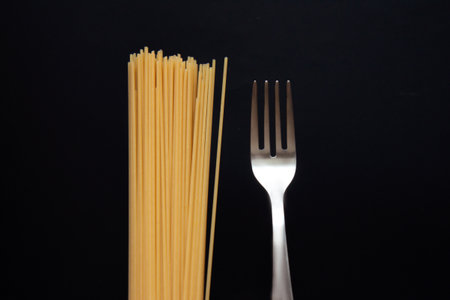 Raw spaghetti with a fork isolated on black background. Pasta. Selective focusの写真素材