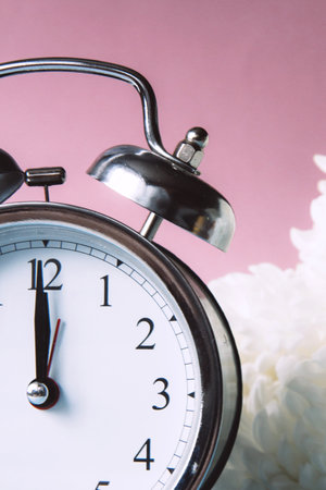 Beautiful vintage silver alarm clock and white peonies on a pink background. Time concept. Holiday...