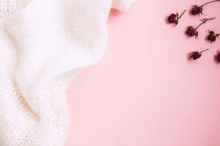 Valentines Day background. Miniature red rose buds and white knitted fabric on pastel pink...