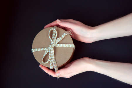 Colorful gift with beige rope in woman's hands on a dark backgroundの写真素材