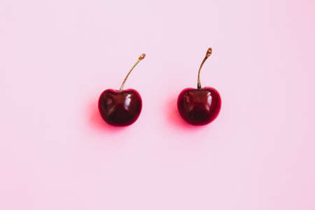 Two ripe cherries on a light pink background. Valentines Day concept. Close-up of cherries. Summer backgroundの写真素材